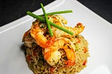 A plate of fried rice garnished with two large shrimps and chives.