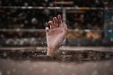 A picture of a hand sticking out of the water as though they’re drowning.