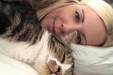 The author lying in bed with her cat sleeping in front of her.