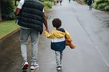 Father and son holding hands, walking down a street.