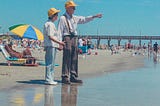 Old man and wife at beach wearing yellow hats