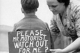 A mother attaches a sign to her son getting ready to ride his bicycle. It reads: ‘Please Mr Motorist. Watch out for me?’