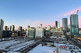 Photo of Calgary city skyline at sunset. Skyscrapers sit underneath a pinky blue sky