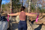 a woman performing resistance band exercises with a pink resistance band outdoors at a campsite