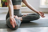 A woman in olive drab yoga clothing seated and practicing a mudra, or yogic hand sign.