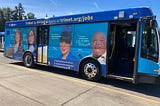 A Gillig 30 foot bus operated by TriMet wrapped with an advertisement about job opportunities at TriMet. The ad features four TriMet employees talking about how much they enjoy working at the transit agency. Cheree, a bus trainer says, “The benefits are awesome, the pay is outstanding.” Caryn, a planning engineer says, “Helping to build the future of transit is rewarding.”