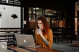 Woman with red hair sipping an iced coffee while using a computer