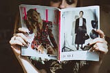 Woman sitting on a chair reading a magazine. She may or may not be in a hair salon.