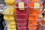 A picture showing stacks of plastic clamshell containers filled with brightly colored cake frosting. Image by Author.