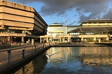 The National Archives buildings reflecting the late afternoon sunshine, with the pond and a swan in the foreground