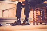 A picture of a man’s legs, he’s wearing a suit, sitting on a pew in a church holding a bible. (He’s supposed to represent a pastor).