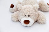 White teddy bear sprawled out face planted on a hard white surface.