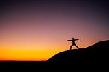 A woman on a hill during sunset doing yoga