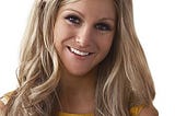 Head shot of Nikki Grahame with her long blonde hair down smiling at the camera. She is wearing yellow.