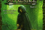 Clad in a dark green hooded cloak, a teenage boy faces the viewer as he holds ready a notched arrow in his bow. Behind him can be seen stout trees, a light green fog pervading the forest in which they stand. ‘Ranger’s Apprentice' appears at the top in large gold text and is underlined by an arrow, followed by ‘Book 1’.