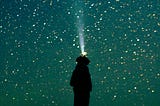 A person shining a flashlight up into the starry sky