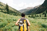 A woman hiking through a meadow toward a mountain valley.