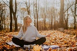 A woman in a gray sweater and leggings meditating in the forest