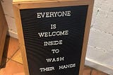 A shop sign stating that everyone is welcome to come in and wash their hands.
