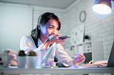 A woman sits at her desk reading her laptop while talking on her phone