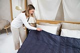 a woman putting a blue blanket on top of a bed