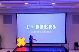 Preet Arjun Singh, host of the Ladders Conference, standing in front of a large screen displaying the conference name.