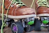 Up close photo of my ruffed up, scuffed up roller skates. Tan boot with a black stripe on the side. Neon green laces. Light green toe stops and black wheels covered in dirt.
