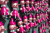 Numerous Pinocchio minifigures with long noses hanging on a wall.