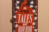 A book titled ‘Tales of Horror’ by Edgar Allan Poe. The book’s cover is dominated with black, red, and white.
