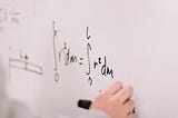 hand writing a mathematical equation on a white board