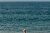 An older woman and a dog facing the vastness of the ocean