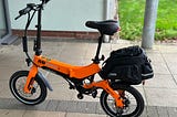 An orange e-bike, MiRiDER brand, with a bike bag on the back rack.