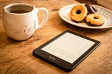 Kobo ereader, donuts, and coffee in a cat mug on table