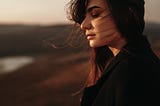 A woman stands alone by a lake.