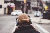 Rearview of a person wearing a beanie and headphones walking down the street.