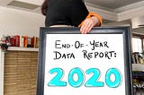 Alyssa (author) stands with back turned to the camera, holding a large frame with the words ‘End of year data report: 2020’