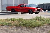 A red El Camino car in a parking lot on a sunny day