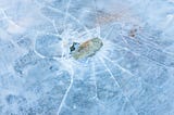 A rock breaking the ice on a frozen lake. This picture descriptive of the phrase “Ice Breaker”.