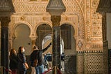 A man in a jacket point upwards at one of the exhibits in a museum, while others are watching and looking at the work