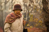 An older woman bundled up for an autumn walk in the forest.
