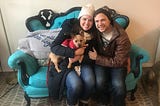 Megan and Tim pose happily with their new dog, Arthur, a Cairn terrier-chihuahua mix, on a blue couch.