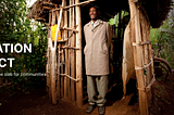 Picture of a person standing in front of a rural setting in front of a bamboo-made bathroom structure, the man is looking upward and smiling positively.