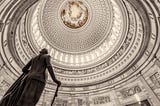 A picture of the U.S. Capitol Building Rotunda, at an angle from the ground up, including the bronze statue of George Washington positioned near the south door of the Rotunda.