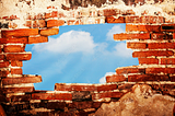 Red brick wall with a hole in the middle. The blue sky with clouds is visible through the hole.