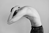 Shirtless man bending with his hands on his neck.