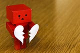 Red paper robot holding a white paper heart torn in half
