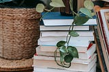 A stack of books with a plant perched on top, its fronds furling down onto the books.