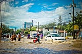 People navigating knee-high water in a flooded city street