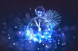 A blue stopwatch, behind are the flash bangs of blue fireworks, and the time om the clock is five minutes to midnight.