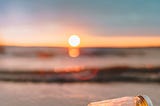 A beach scene at sunset. A glass jar sits on its side. Enclosed are a string of fairy lights.